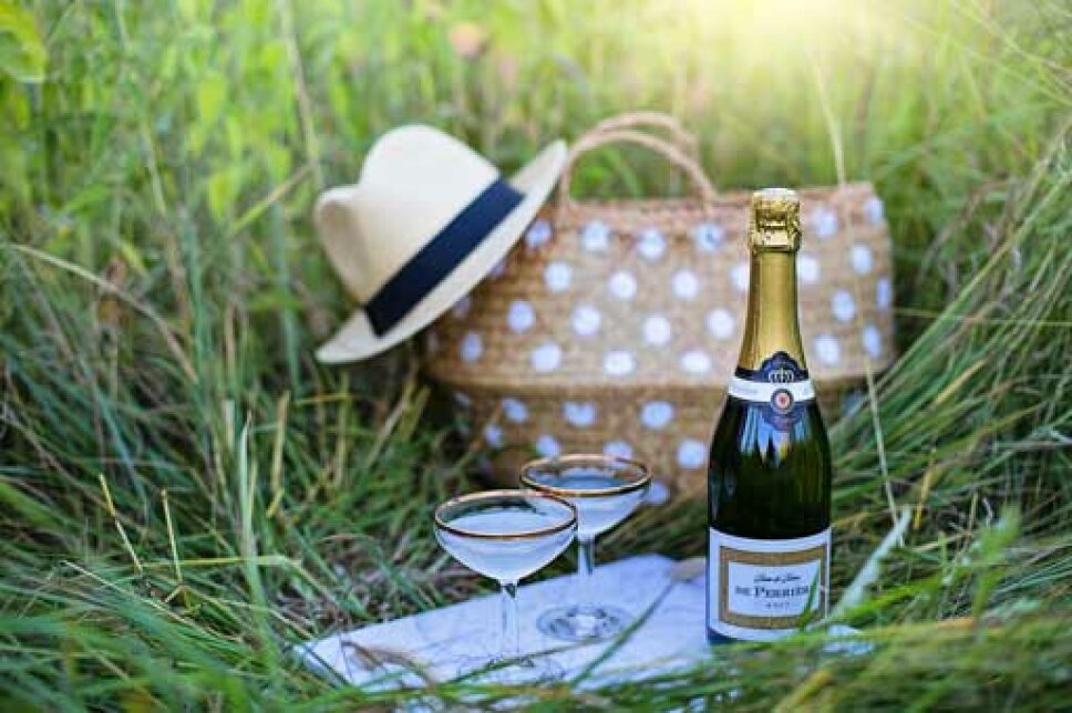 ein Picknickkorb sowie Sektgläser und Sektflasche stehen im Gras
