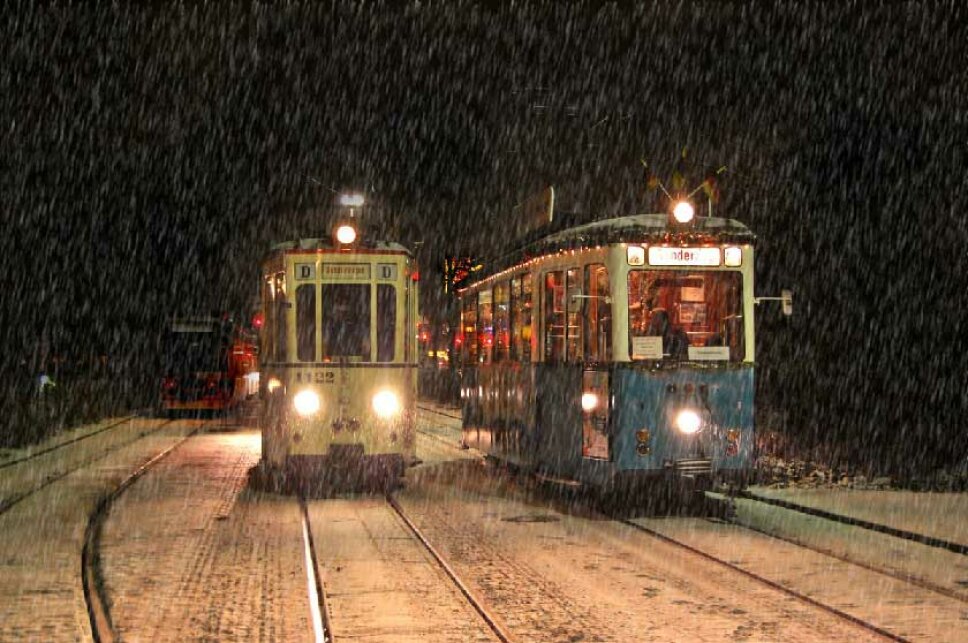 2 historische Straßenbahnen fahren auf einer verschneiten Strecke