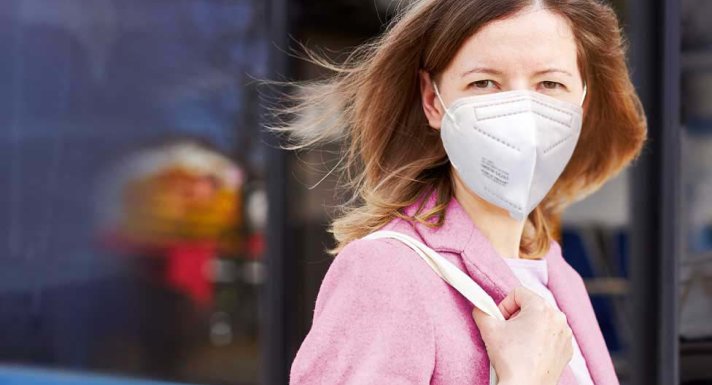 Frau mit FFP2-Maske vor einer Straßenbahn